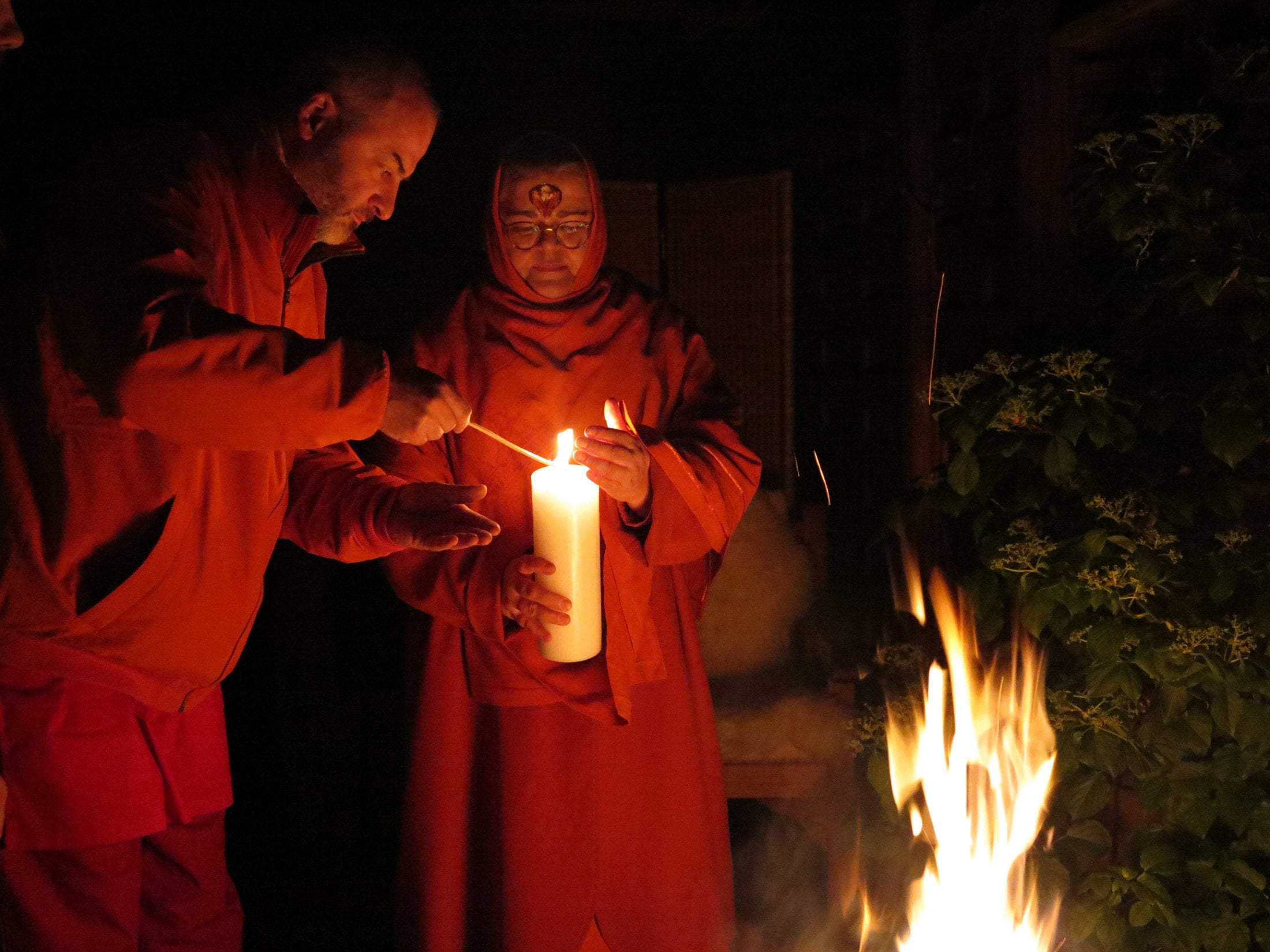 Laxman entzündet die Kerze in Ma's Hand. Anschließend trägt Ma das erste Licht ins dunkle Darshanzimmer.